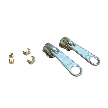 A set of brass zippers with pulls and stops laid out on a white surface.