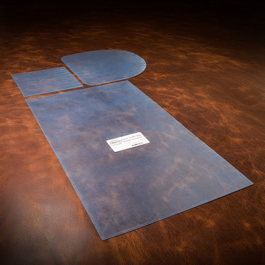 A set of blue acrylic templates used for creating a custom duffle bag out of leather, laid out on a textured brown leather background.