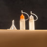 2 plastic paint dropper bottles with colored caps, used for applying small amounts of paint or finish, displayed on a brown leather surface in front of a dark background.