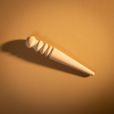 A wooden edge slicker for leather projects laid out on a textured light brown leather background.