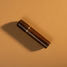 A wooden needle box with a gold colored metal accent, used for storing sewing needles, displayed on a textured light brown leather background.