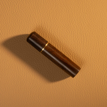 A wooden needle box with a gold colored metal accent, used for storing sewing needles, displayed on a textured light brown leather background.