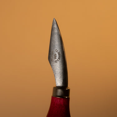 A `bleeder' tool, used for leather crafting and tooling. Laid out on a solid brown background.
