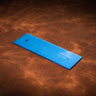 A blue acrylic template used for creating a custom ribbon wallet made from leather, laid out on a brown leather textured background.