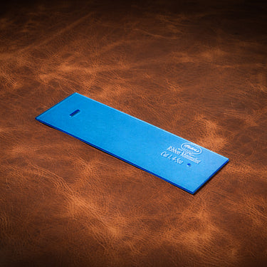A blue acrylic template used for creating a custom ribbon wallet made from leather, laid out on a brown leather textured background.