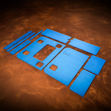 A set of blue acrylic templates used for creating a custom pony express satchel made of leather. Laid out on a textured brown leather background.