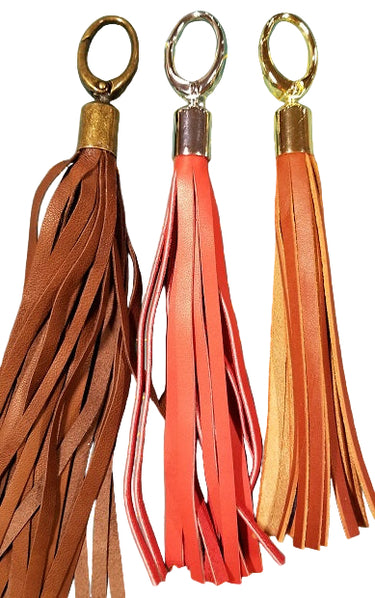 Three leather tassel clips in brown, red, and orange, with metal clasps on the top, displayed against a white background.