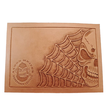A tooling pattern featuring a skull and spider web design, embossed onto a leather material.