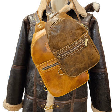 A brown leather sling bag displayed on a mannequin wearing a black jacket.