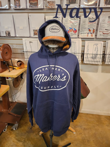 A navy blue hoodie with a maker's leather supply logo, standing on a mannequin in a leather workshop.