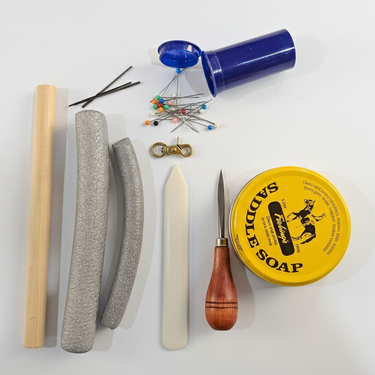 Collection of items including some saddle soap, a wooden tool, and other leather tools and accessories on a white background.