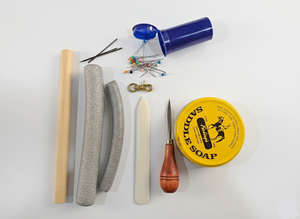 Collection of items including some saddle soap, a wooden tool, and other leather tools and accessories on a white background.