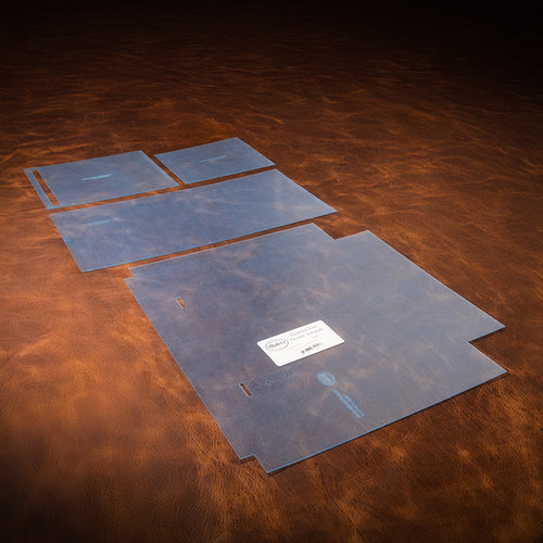 A set of blue acrylic templates used for creating a custom tote bag made of leather. Laid out on a textured brown leather background. 