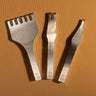 A set of 3 buck-stitching chisels used for stitching with leather projects in the small size. Laid out on a light brown textured leather background. 
