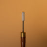 A paint roller tool with a textured metal tip and sturdy wooden handle, used for applying paint to leather surfaces, laid out on a solid light brown background. 