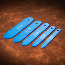 Load image into Gallery viewer, A set of blue acrylic templates used for creating custom belt ends made from leather. Laid out on a textured brown leather background. 
