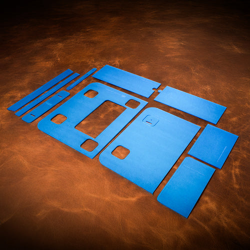 A set of blue acrylic templates used for creating a custom pony express satchel made of leather. Laid out on a textured brown leather background. 