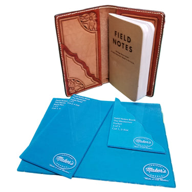 A brown leather notebook cover with a 'FIELD NOTES' embossed on it, displayed on a cutting mat, alongside two blue acrylic templates.